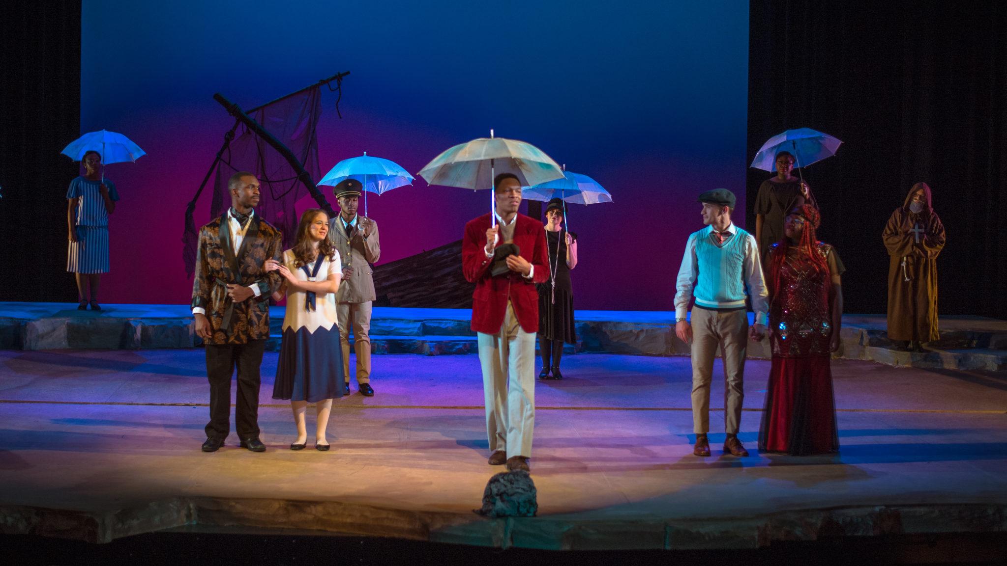 Cast of Twelfth Night on stage, some holding umbrellas